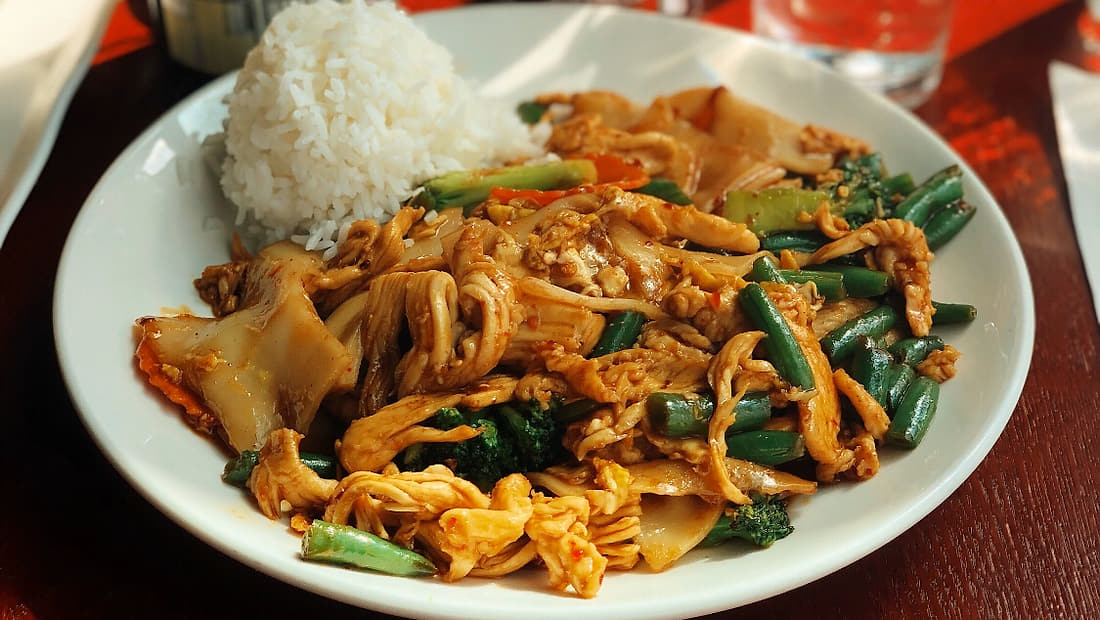 Plate of wok-fried noodles with chicken, green beans and rice