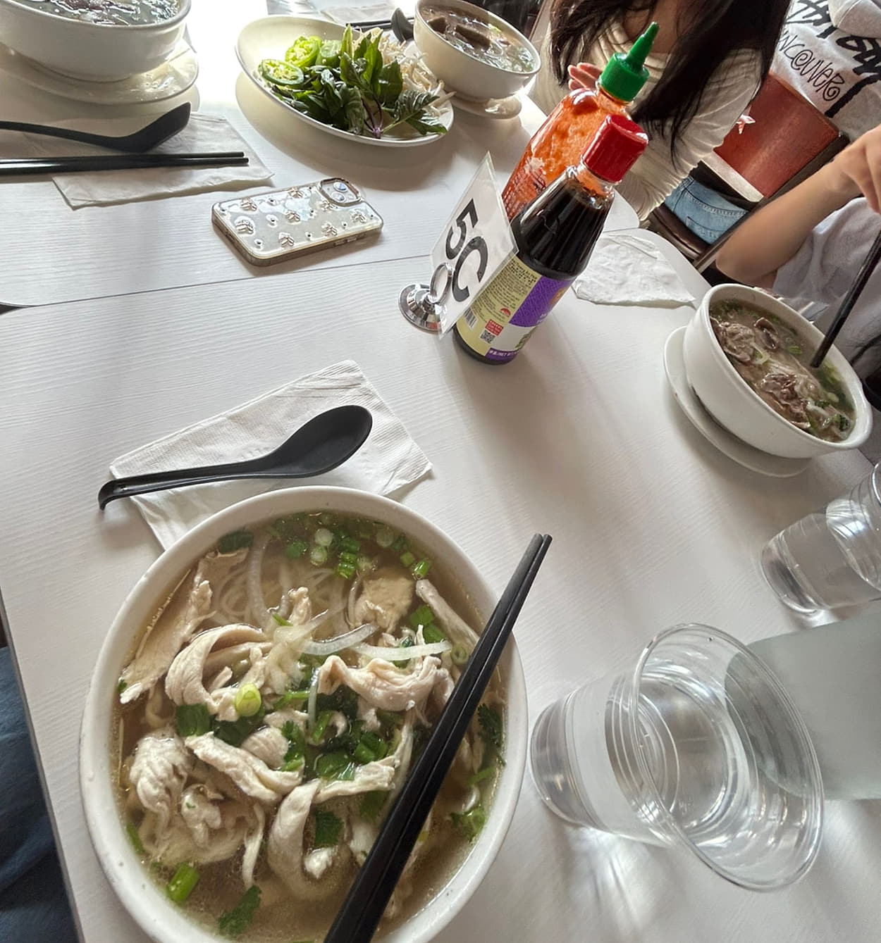 A table at Basil Viet Kitchen in Seattle with a bowl of pho, a plate of herbs and hot sauce